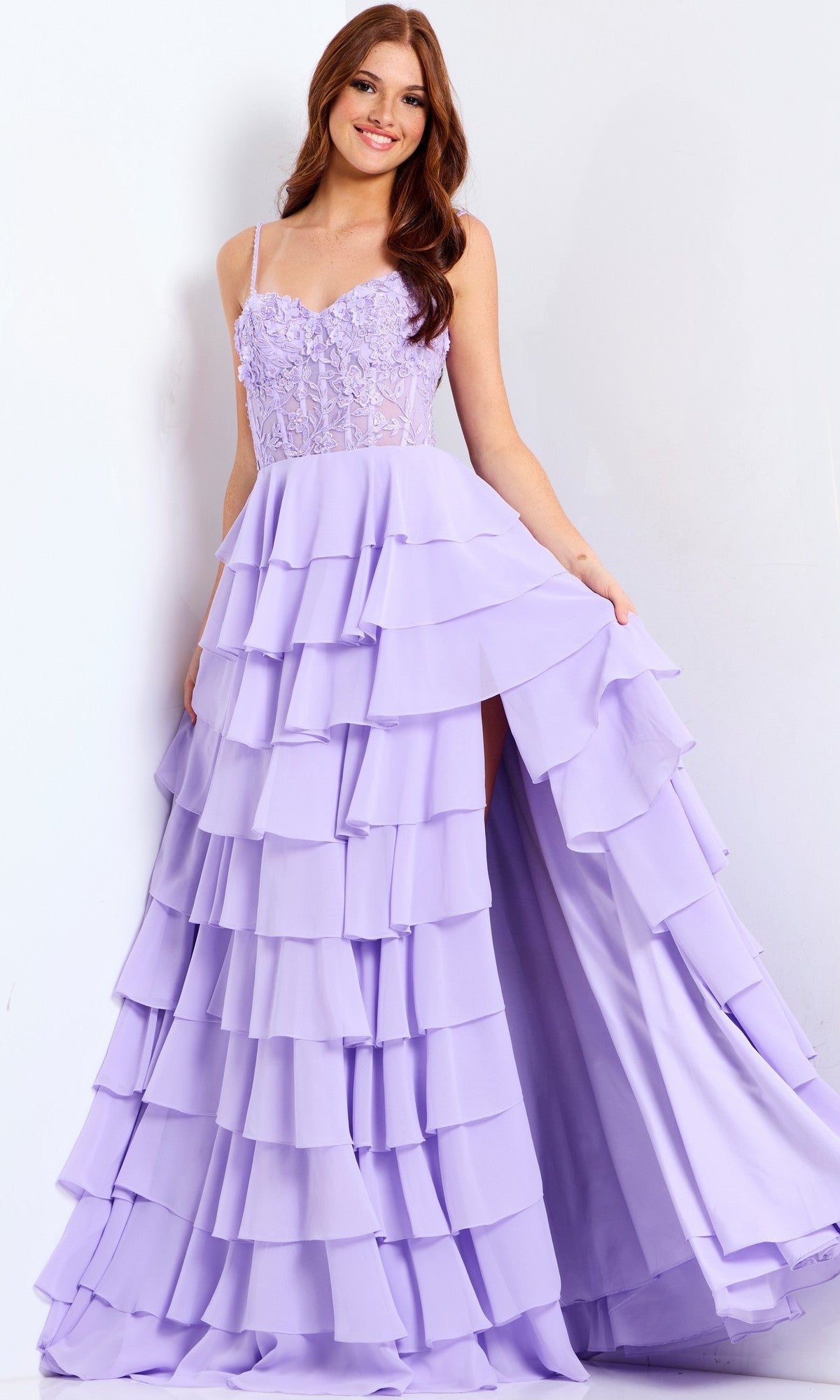 A woman in the Jovani 44543 lilac long prom dress with a lace corset bodice, sheer straps, and tiered ruffle chiffon skirt stands against a white background.